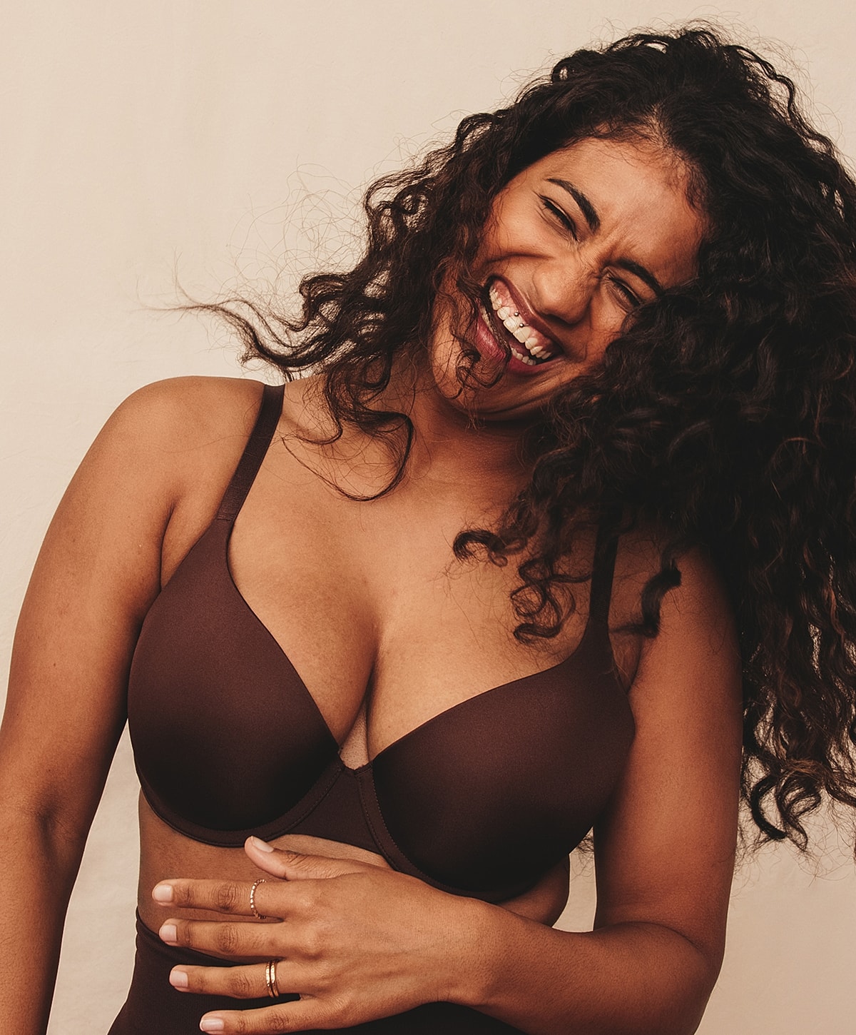 Smiling woman wearing a brown bra, curly hair.
