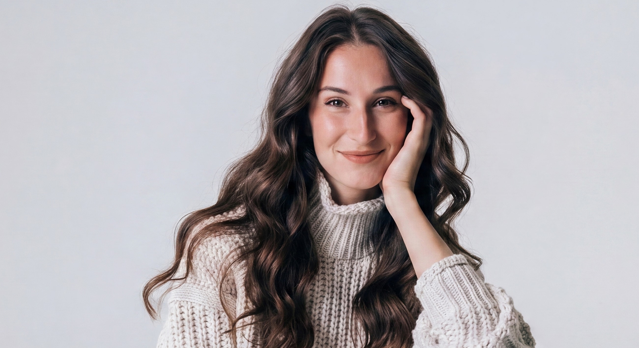 Smiling woman with long, wavy hair, cozy sweater.