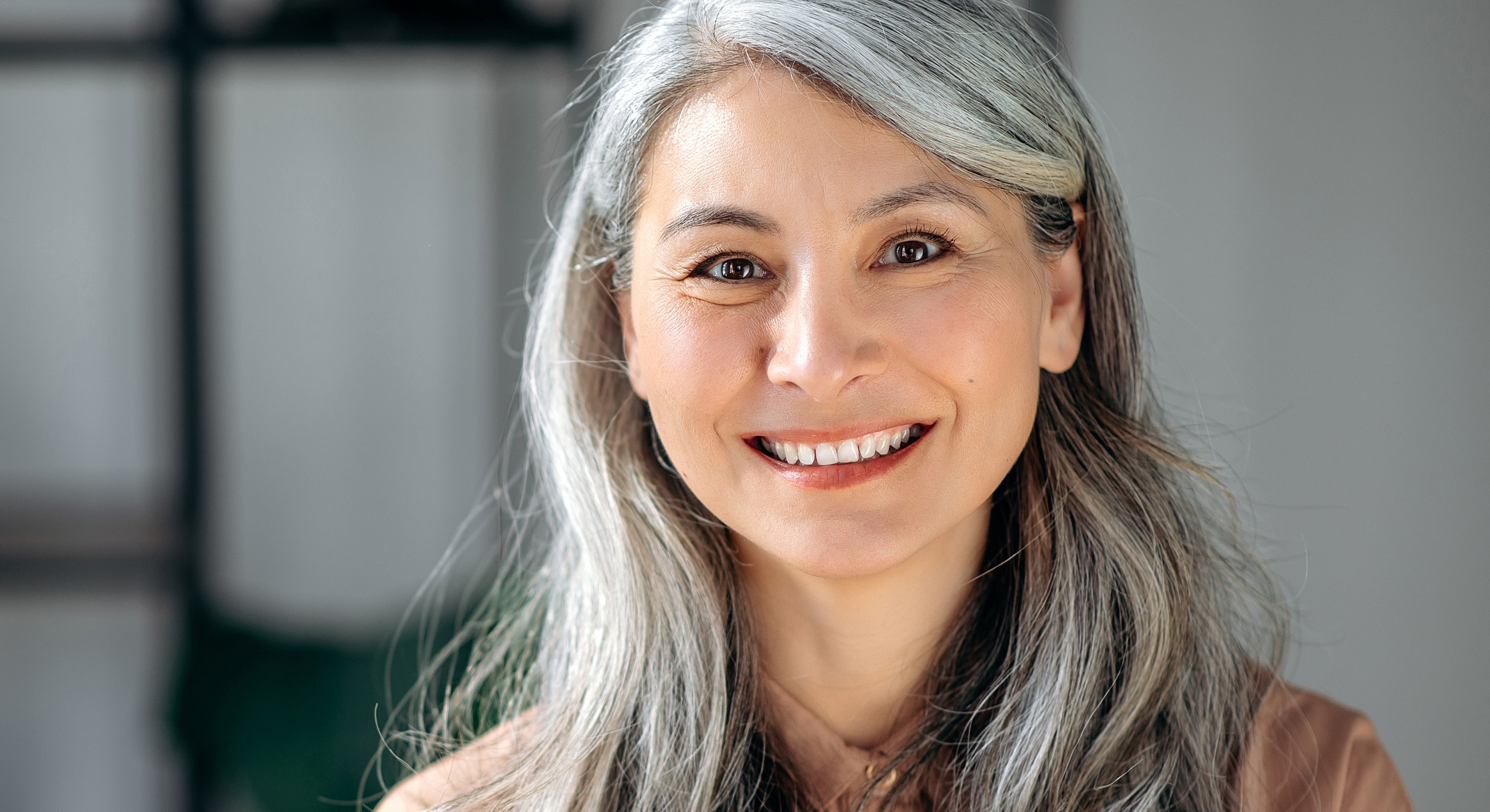 Smiling woman with long gray hair indoors.